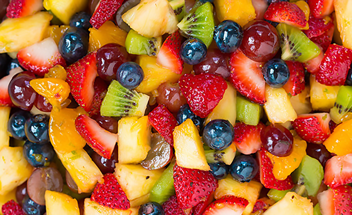 A fruit salad made of tangerine wedges, blueberries, strawberries, pineapple, kiwi, and grapes fill the entire frame. The strawberries, kiwi, pineapple, and grapes are all cut into smaller pieces. The skin of the blueberries and grapes is shiny and wet from the fruit juice.