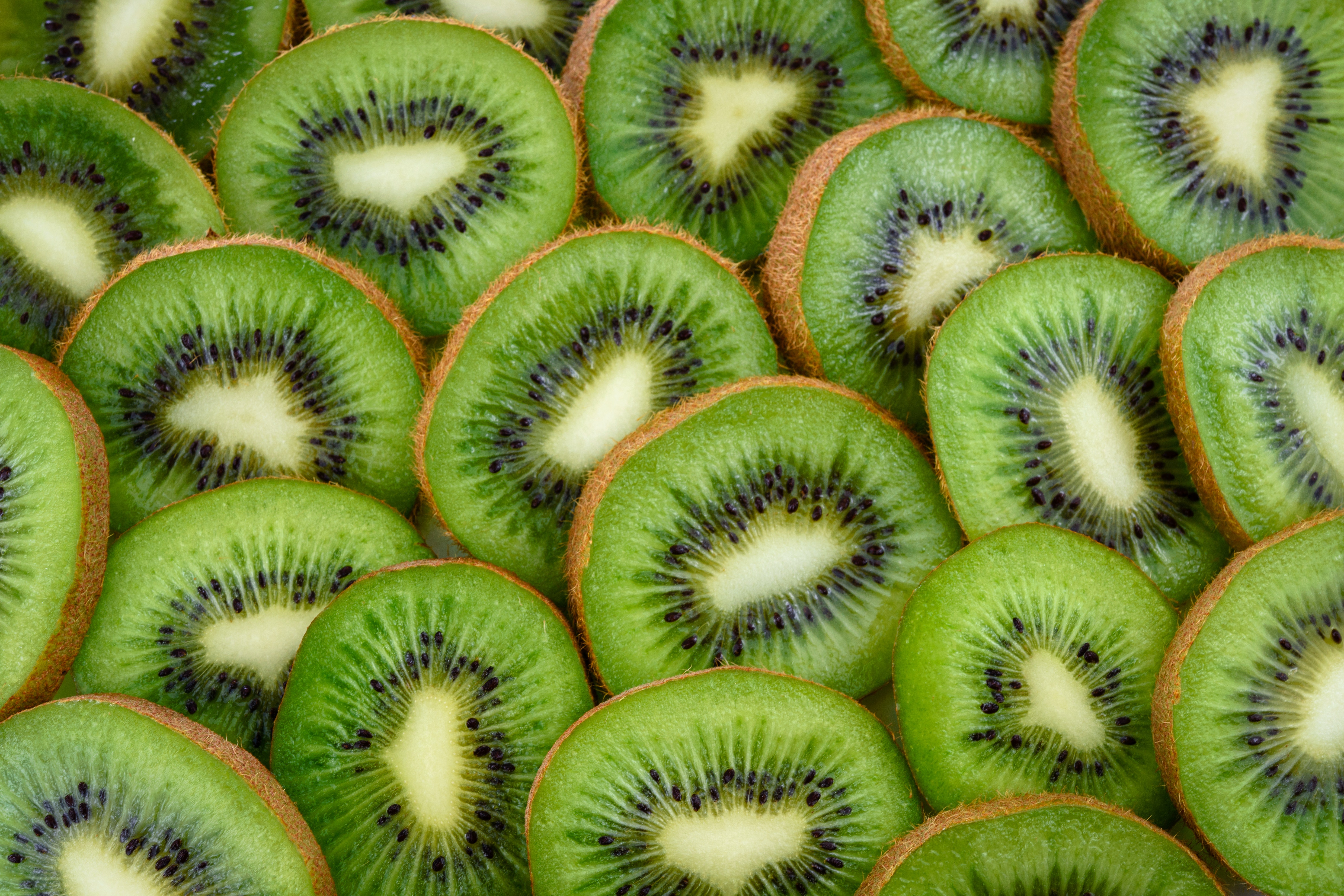 A pile of kiwis cut in half with seeds facing the camera.